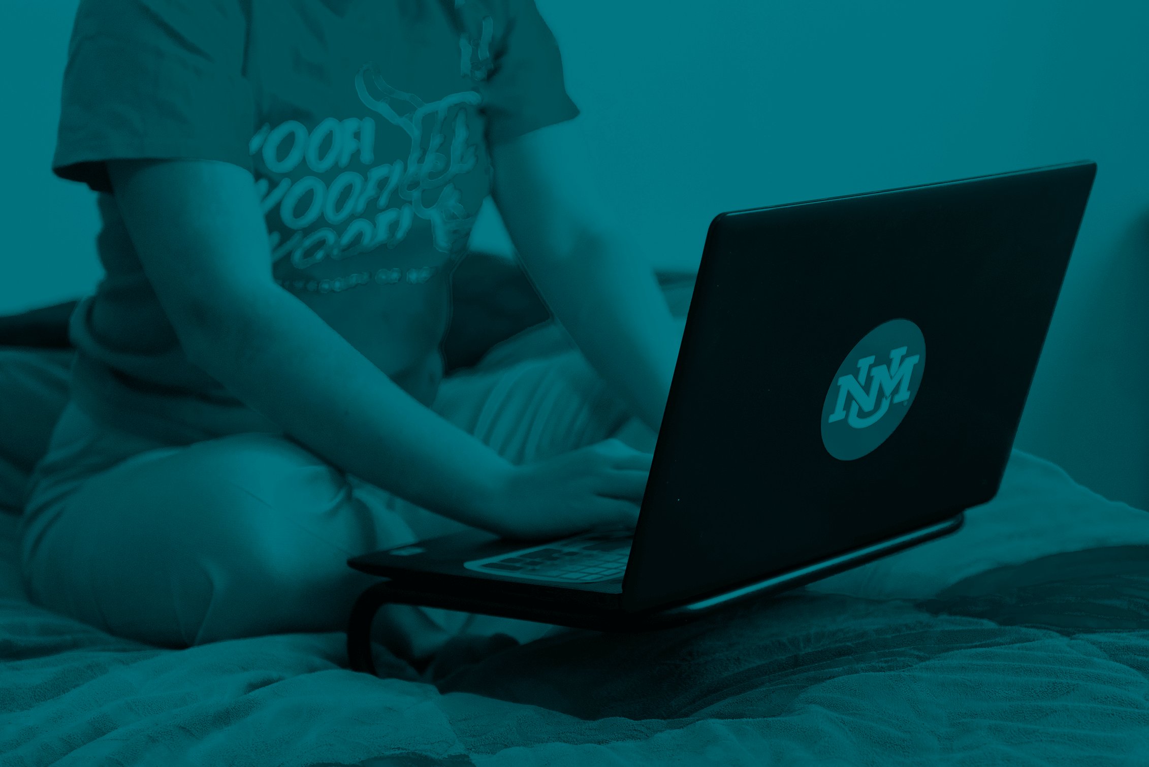 student seated on bed using laptop